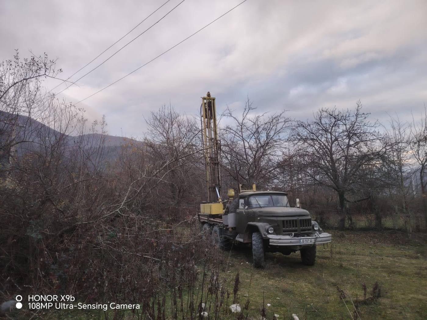 Тяжёлая советская буровая установка с высокой мачтой на шасси грузовика в сельской местности у Амбролаури в сумерках, Грузия