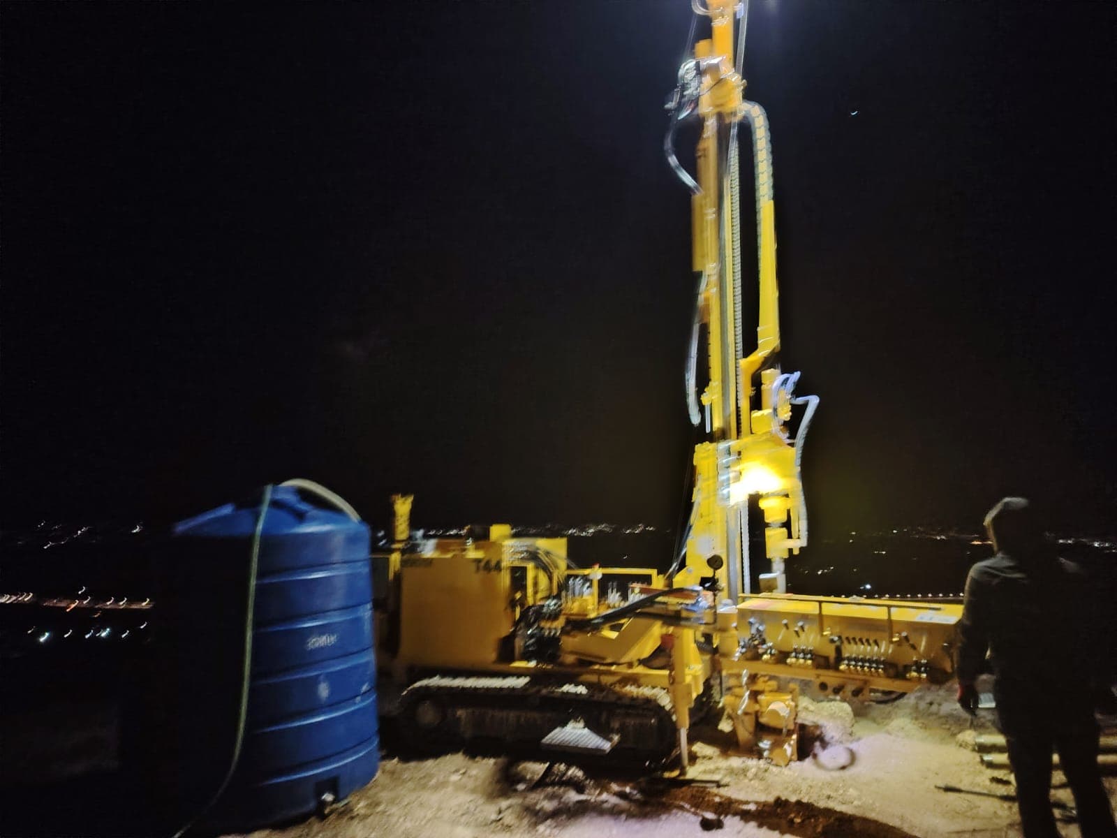 Night borehole drilling operation with panoramic view of Kutaisi city lights, geotechnical field work in Georgia