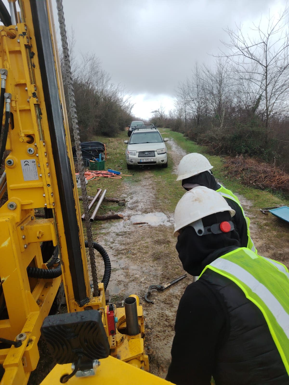 Two geologists in safety gear supervising borehole drilling for wind turbine project near Kutaisi