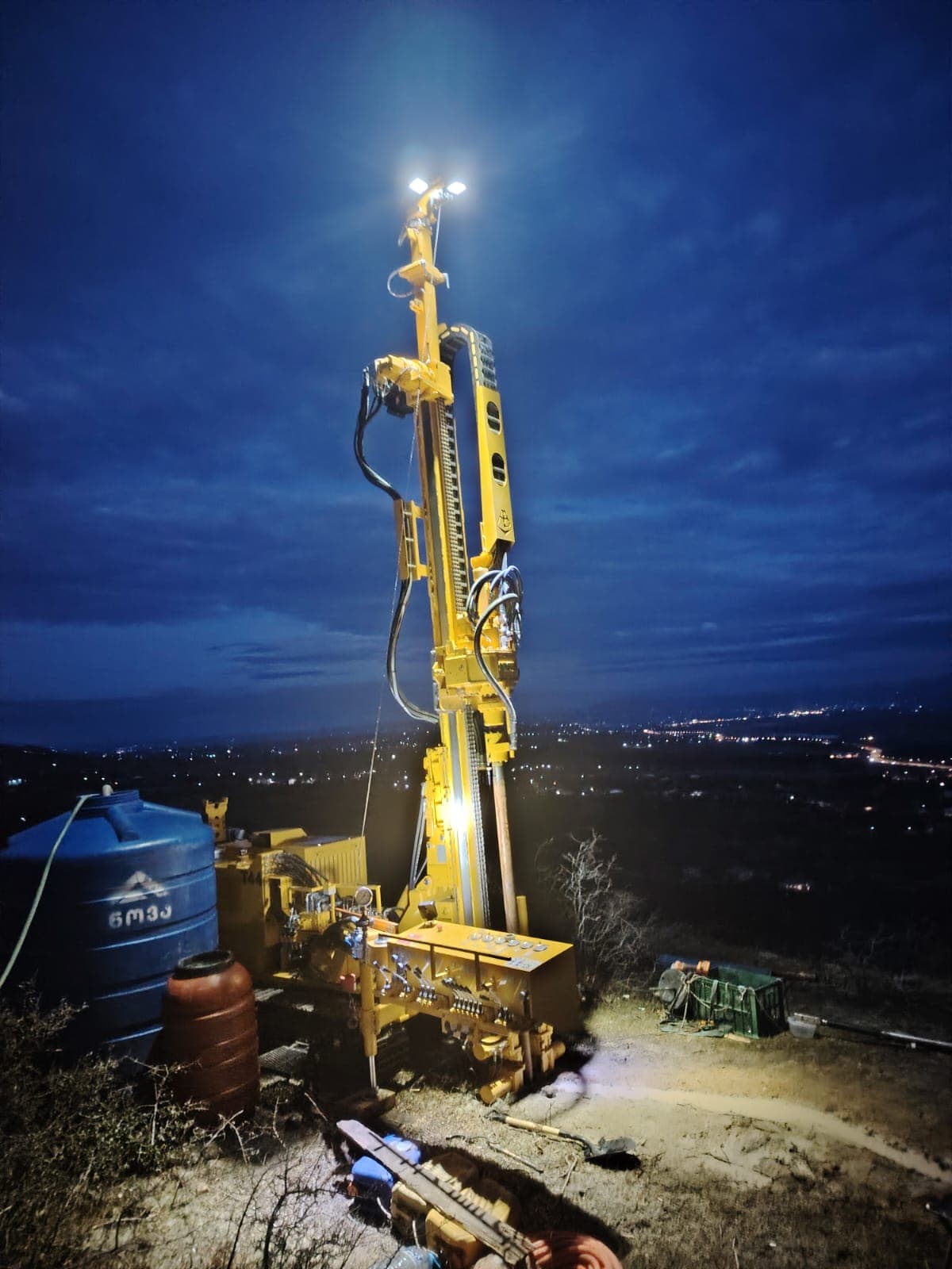 Geotechnical drilling rig on hilltop at dusk overlooking Kutaisi, geological survey for wind energy project